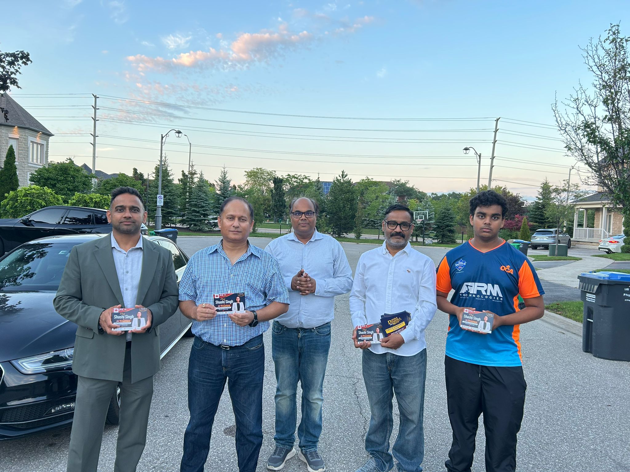 Volunteers holding Elect Shashi Singh for Trustee campaign flyers in a Mississauga neighbourhood at dusk