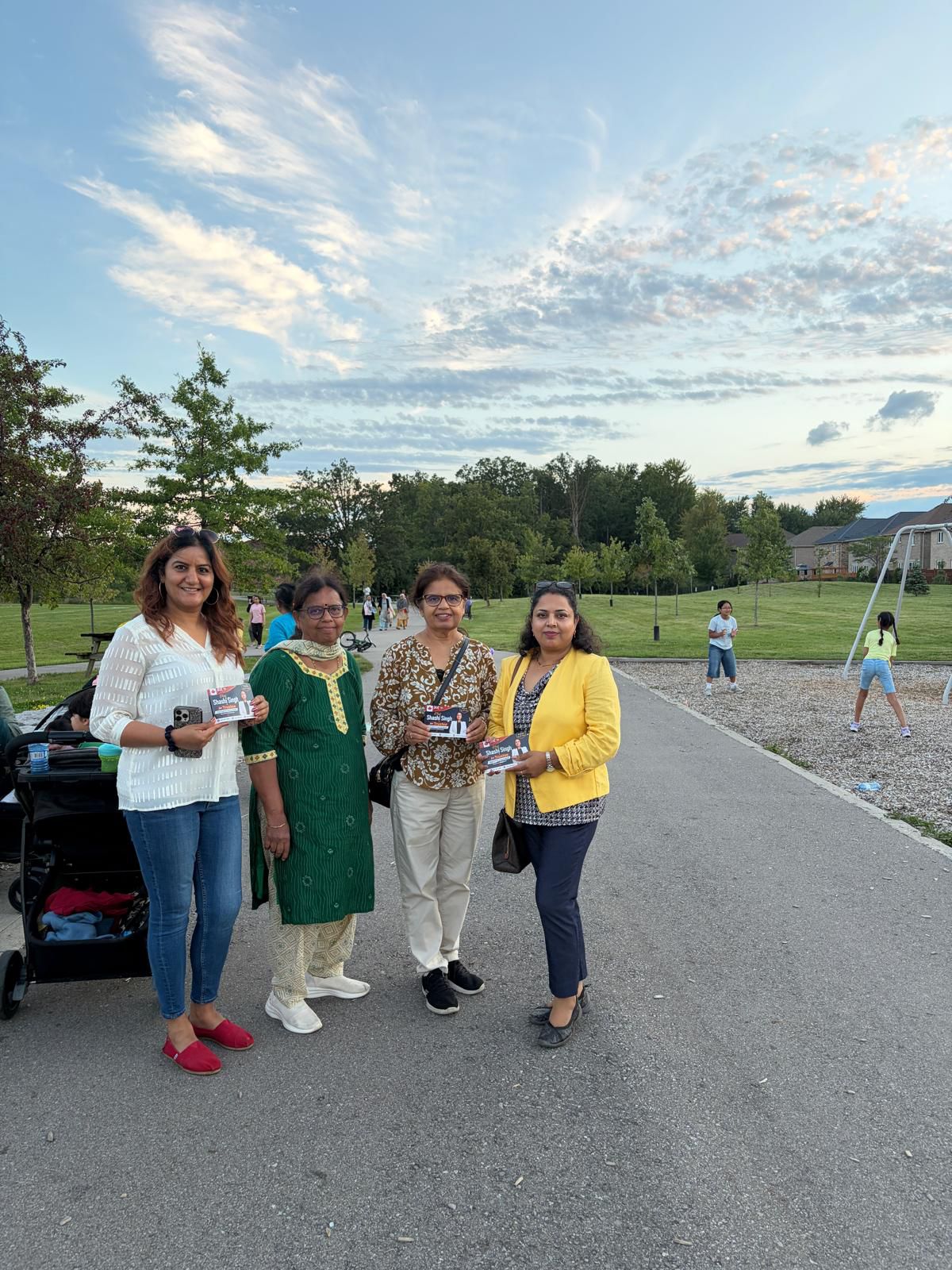 Community members holding Elect Shashi Singh for Trustee flyers on a park pathway near a playground